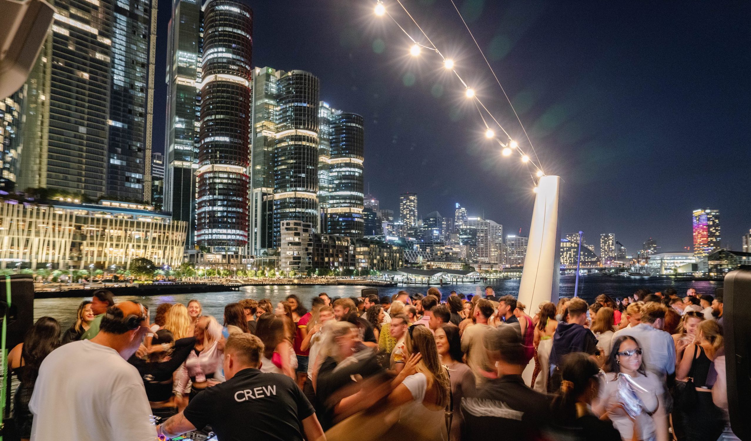 Harbour party crowd beneath illuminated city skyline