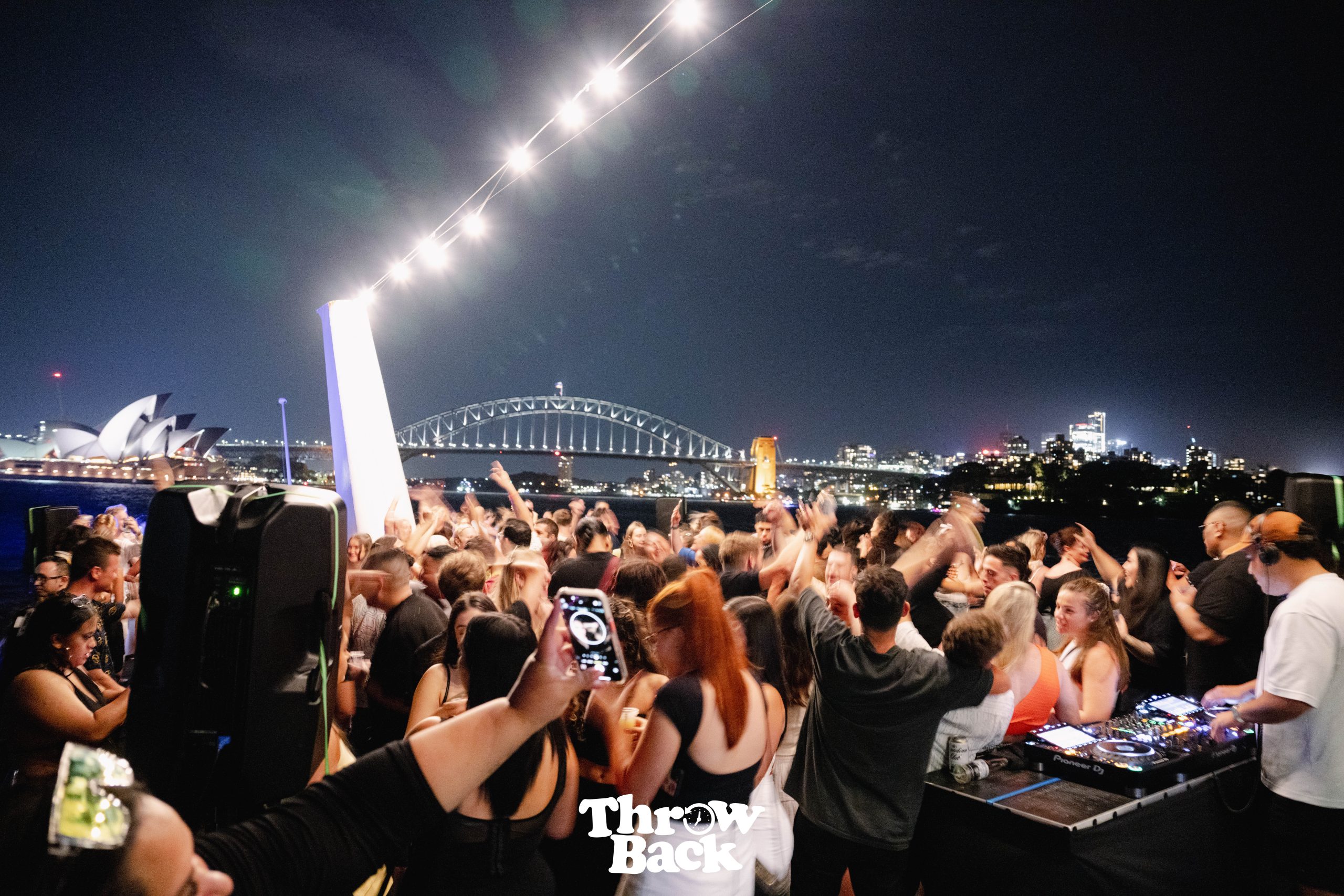 Harbour party crowd beneath illuminated bridge lights