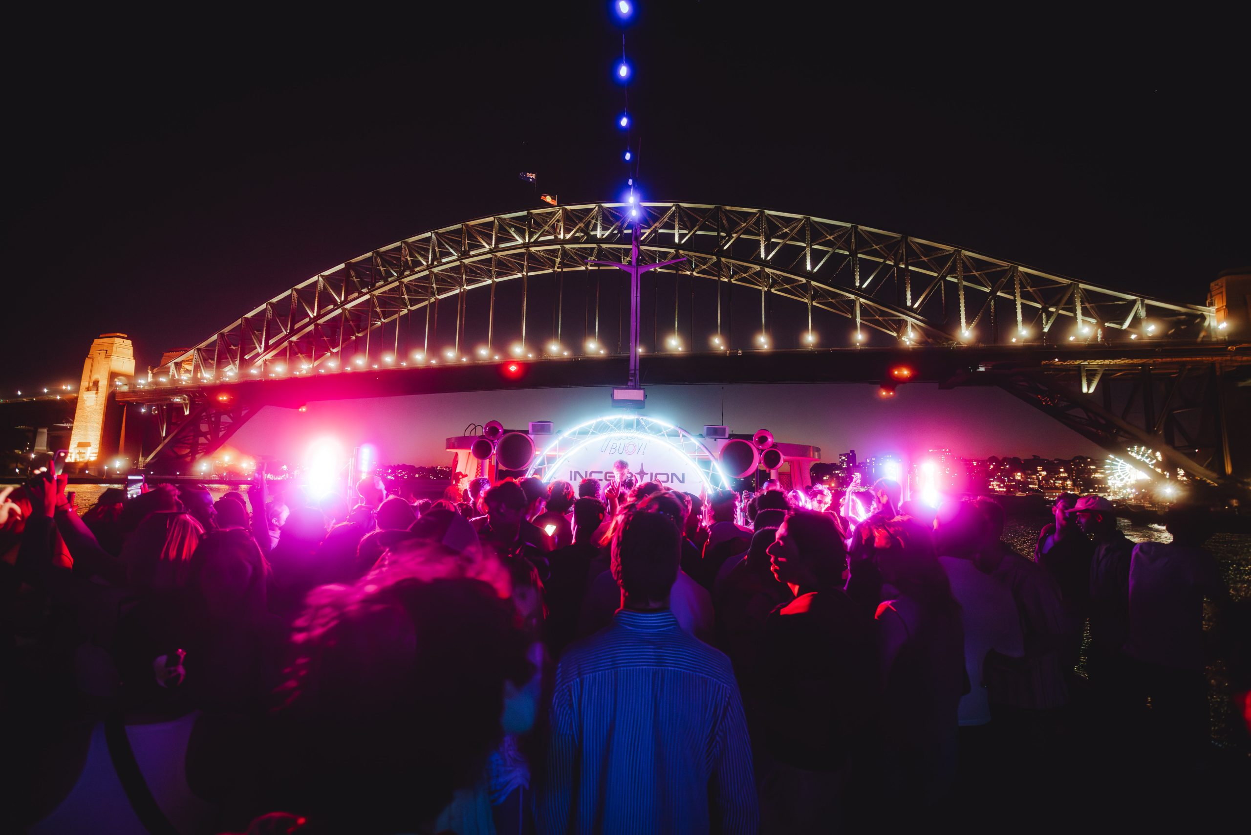 Night-time party crowd beneath the illuminated Harbour Bridge